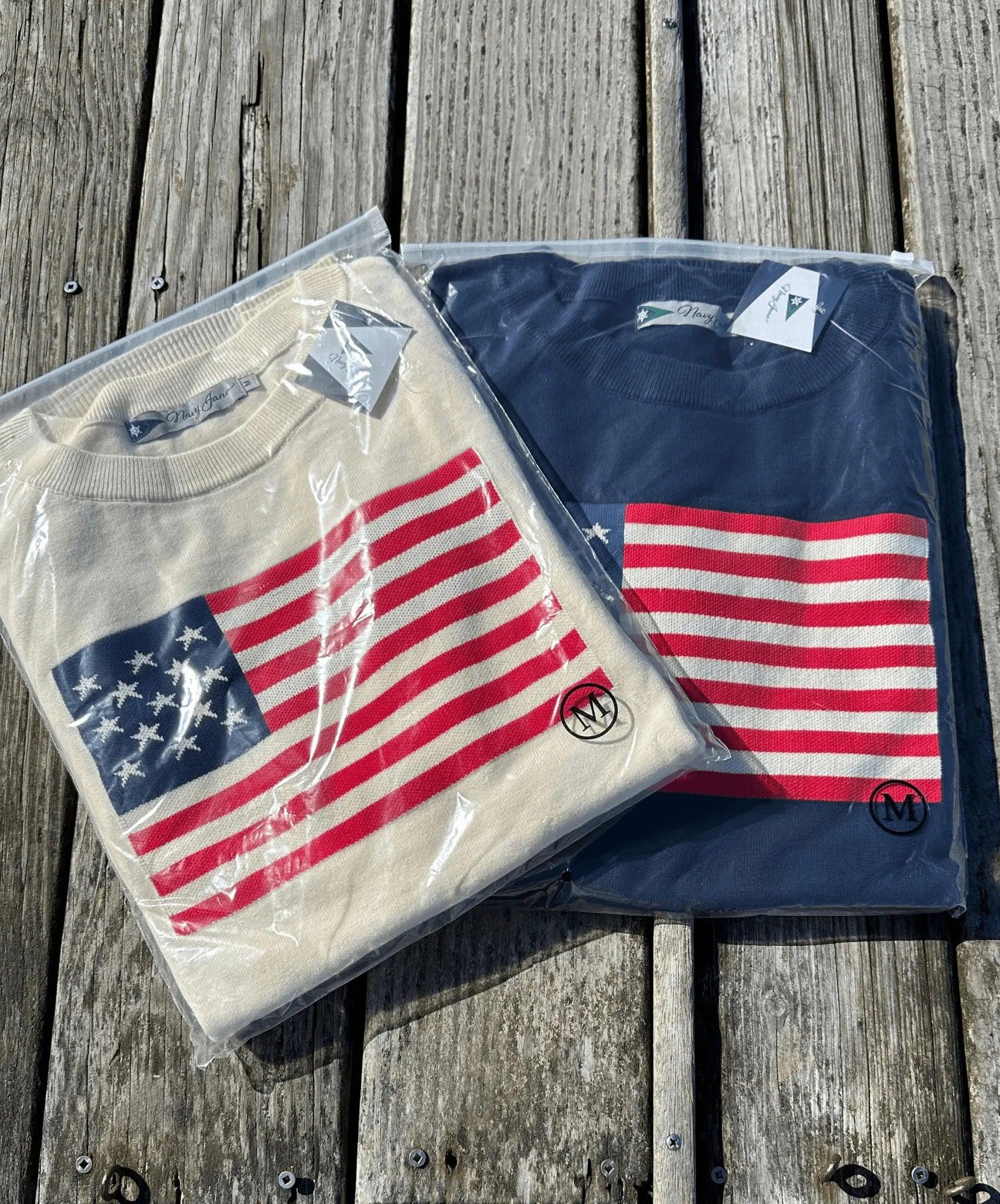 Picture of a navy sweater with American Flag sweater. Also a picture of a cream sweater with an Americna Flag. Both still in clear packages.