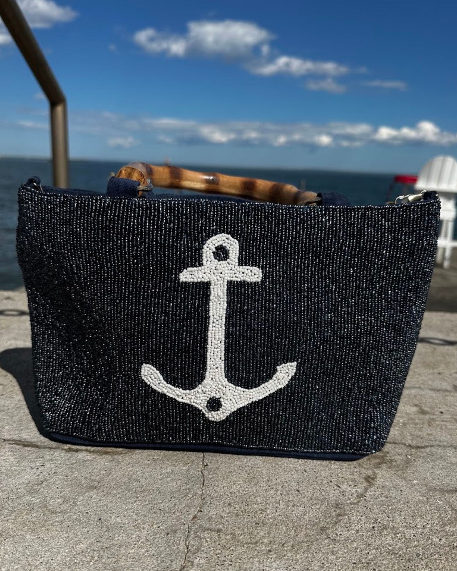 Beaded Navy blue bag with a white anchor design on a concrete surface by the water.