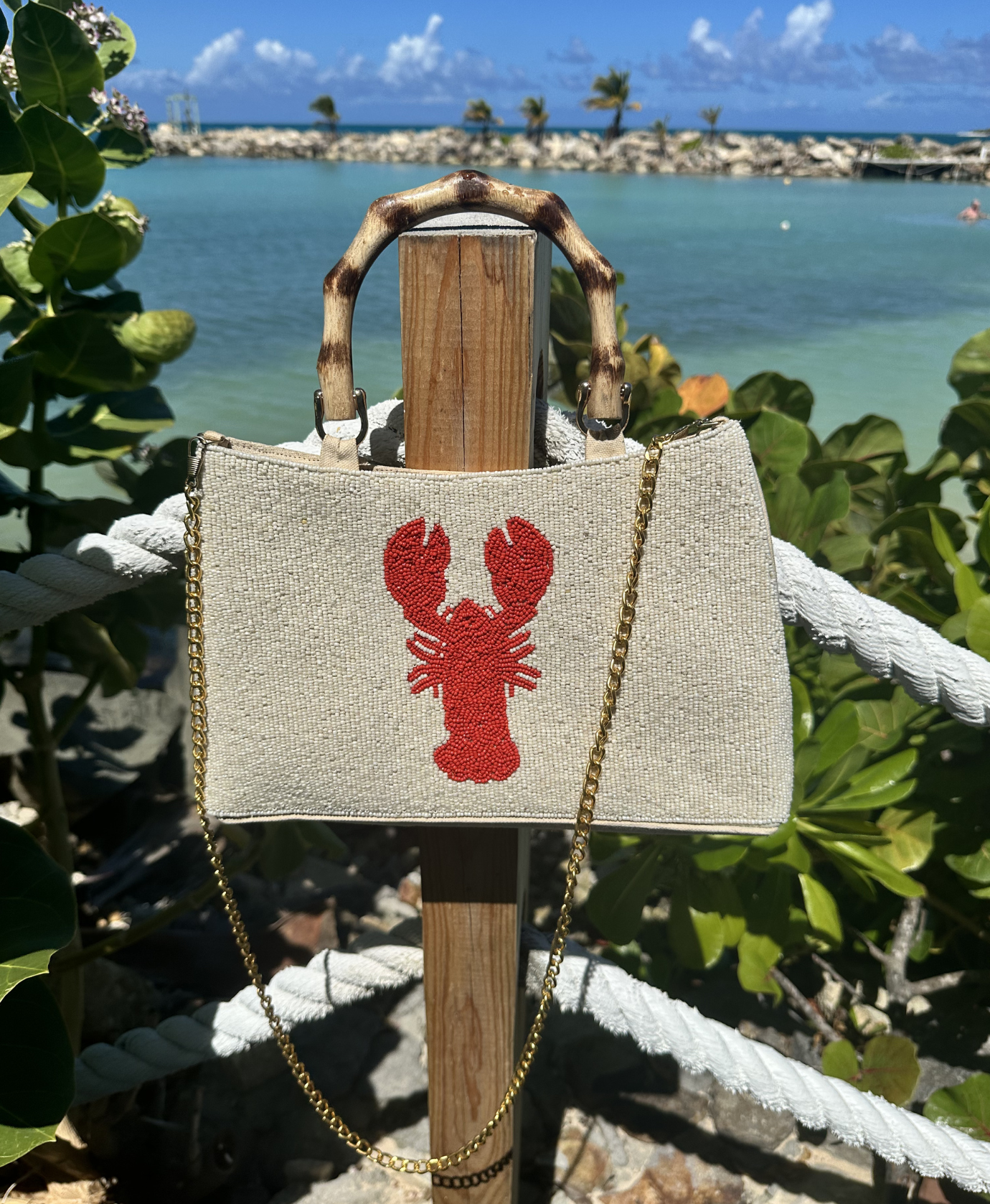cream beaded purse with curved bamboo handle, gold chain, and red lobster design,