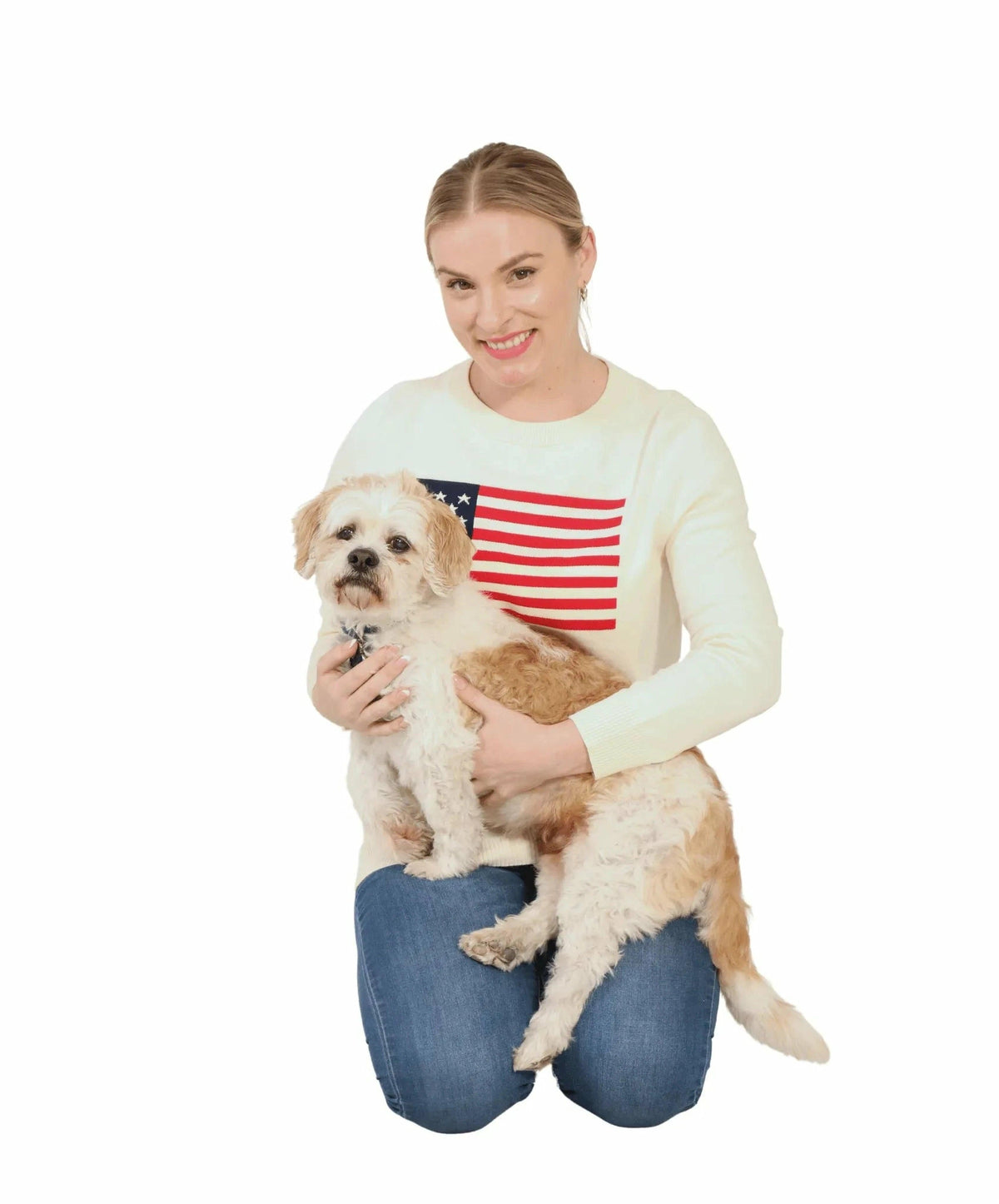 Girl wearing cream sweater with American Flag holding a small dog with a clean white background