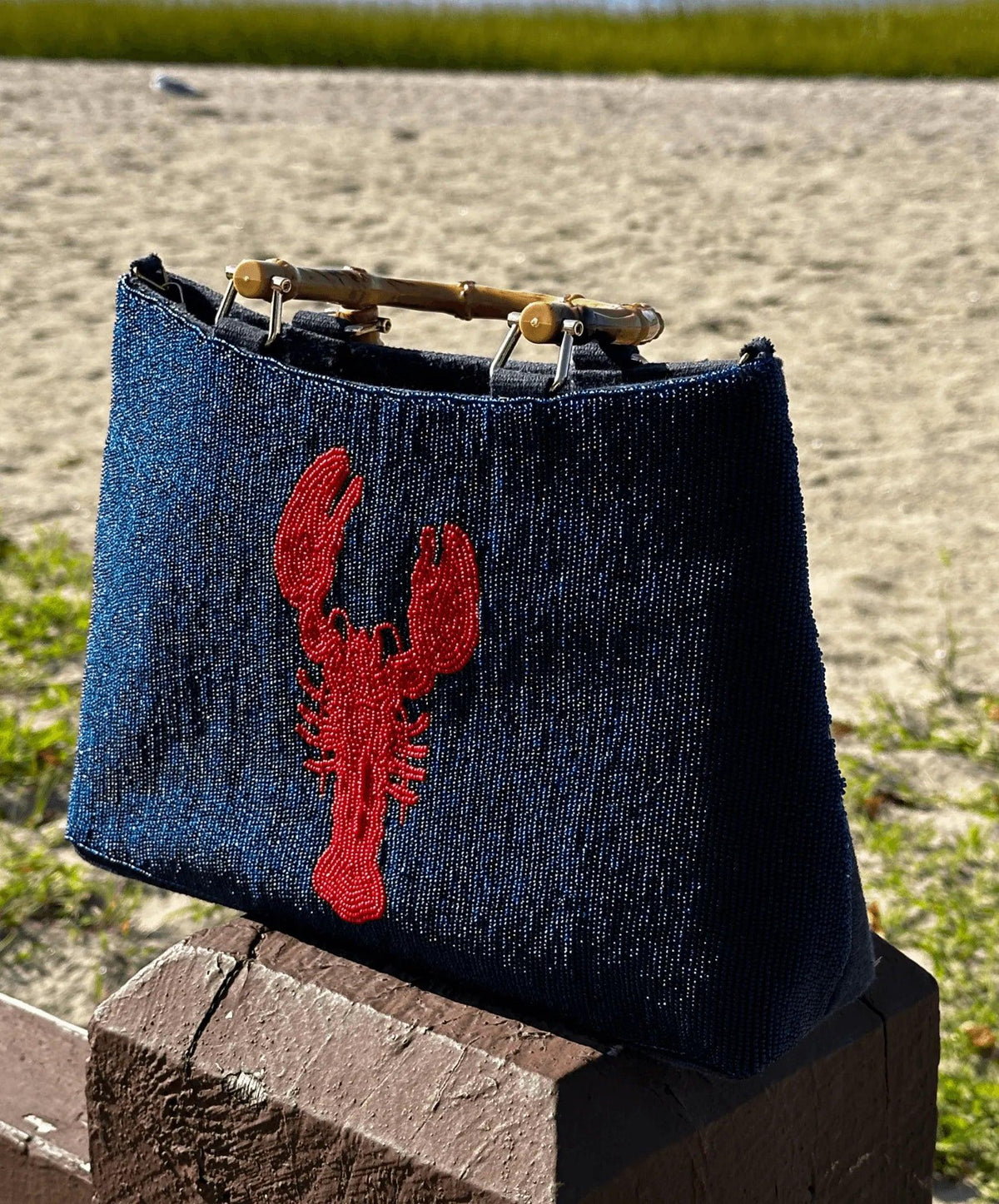 side view of navy beaded lobster handbag with bamboo handles.  It's sitting on a post right by the water.