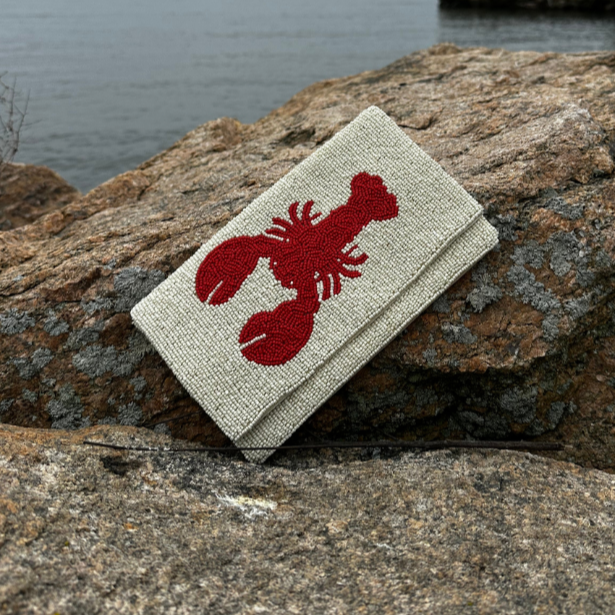 Cream Beaded Clutch with a Red lobster desig on a rocky surface by a body of water
