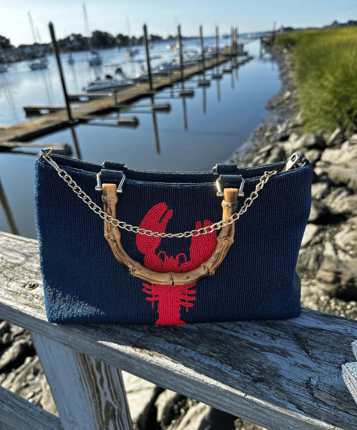 Picture of navy beaded purse with red design.  Bamboo handles and gold chain.  Sitting on railing by the water.  