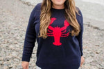 close up of Woman wearing a navy sweater with a red lobster design on a rocky beach.
