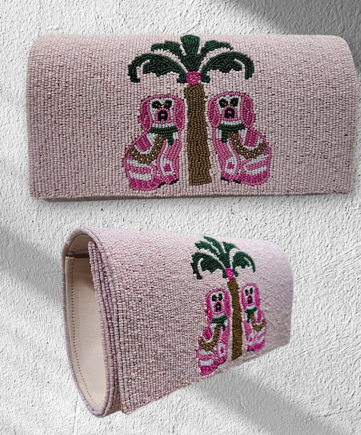 A luxury clutch with a pink background featuring a beaded chinoiserie dog design beneath a palm tree.