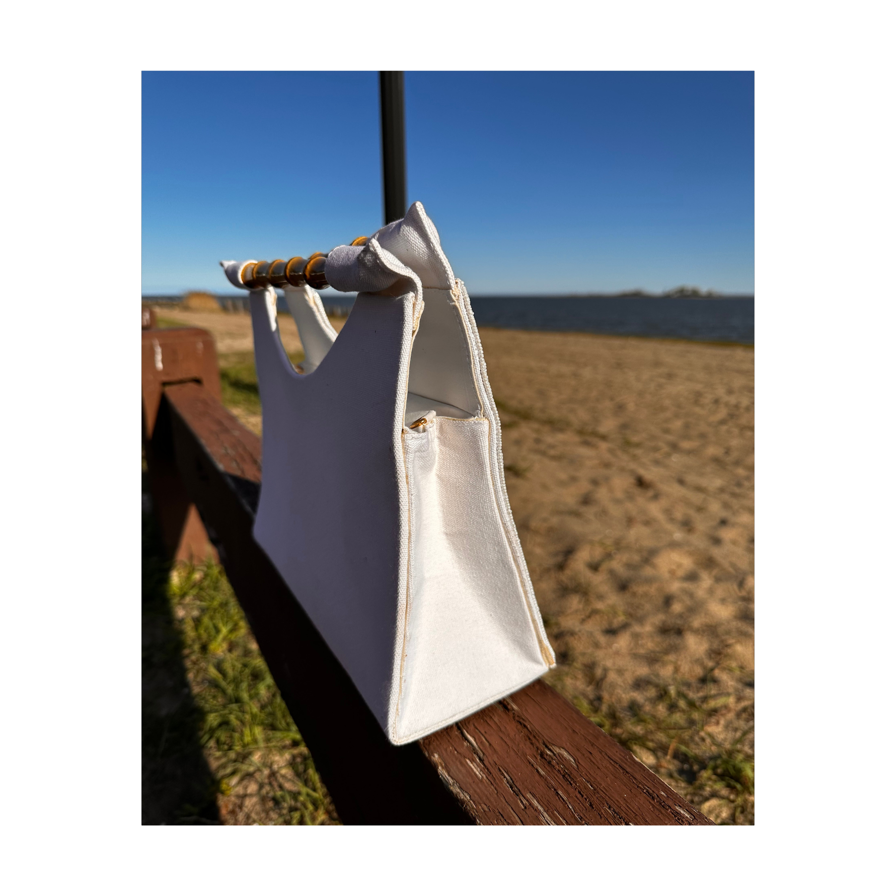 Side view of white beaded purse with sailboat design, beach background.