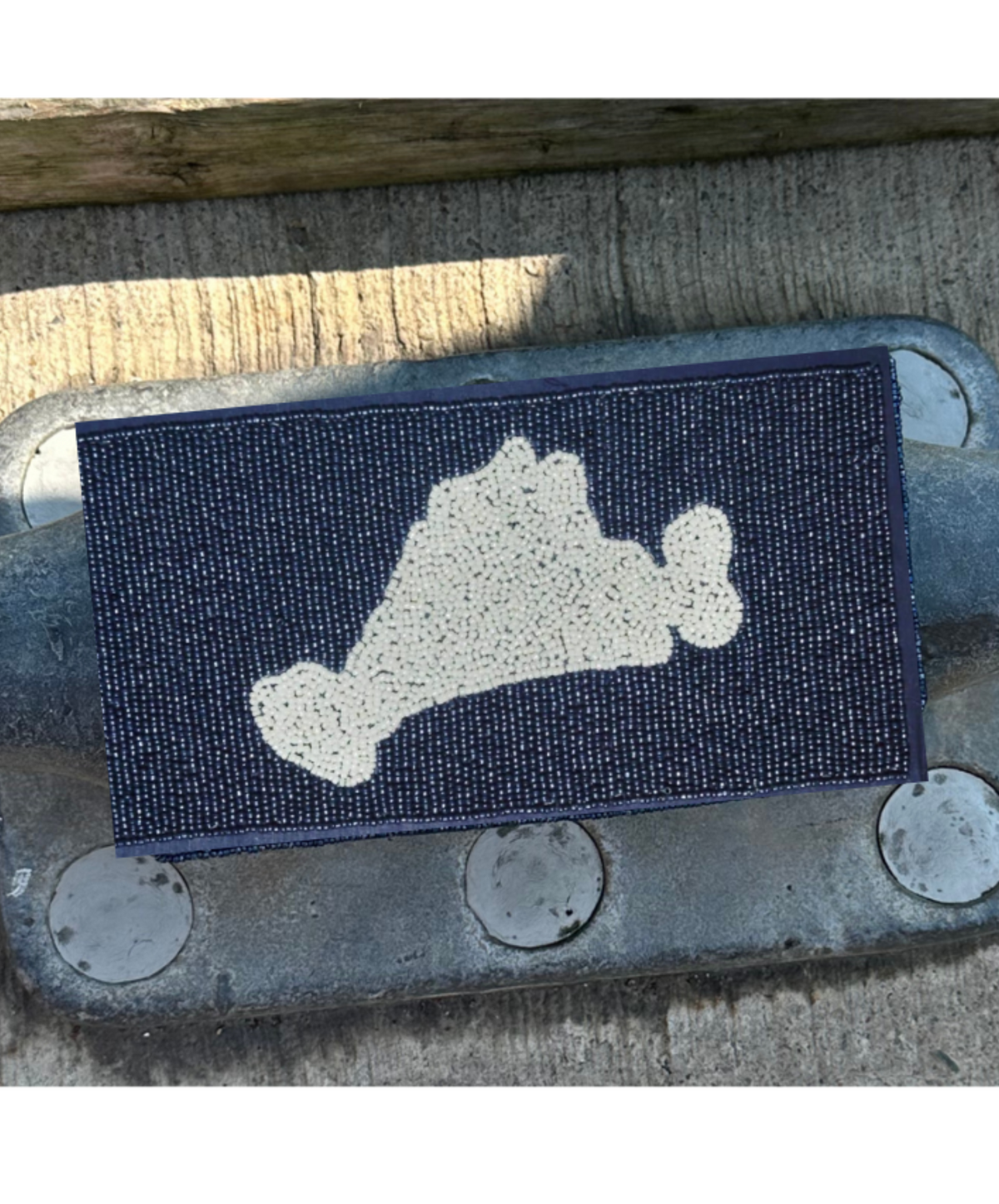 Navy beaded purse with white marthas vineyard image.  Leaning agains a silver cleat. 

