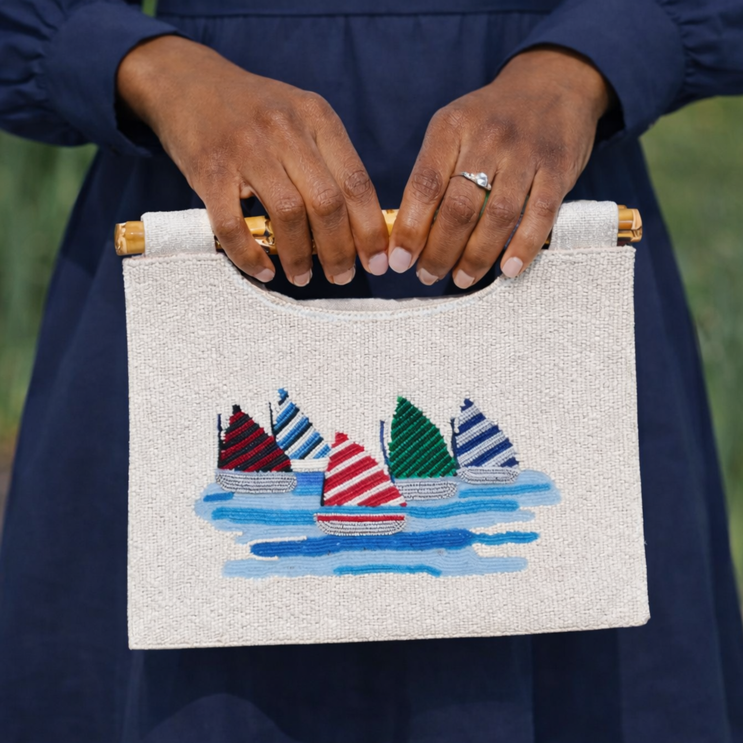 Person holding a handbag with embroidered sailboats design against a blurred background